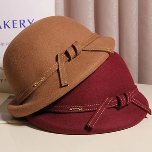Detail of wool cloche hats with decorative bows and metal logos in camel and dark red