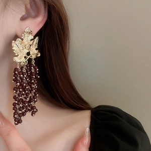 Macro detail of leaf-shaped earrings with cascading deep red bead tassel fringe