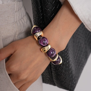 Dettaglio di perle in acrilico viola marmorizzato e distanziali dorati su un bracciale