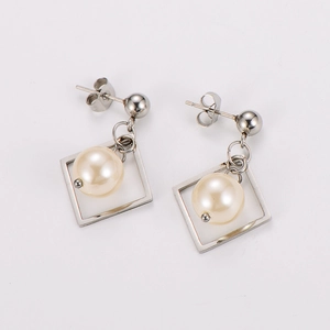 Macro shot of silver hollow square stud earrings with creamy faux pearl on white surface
