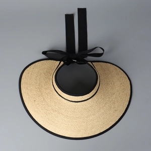 Detail of beige raffia sun visor featuring a black trim and elegant ribbon bow tie
