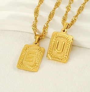 Macro view of gold 18K stainless steel square pendants with embossed letters E and U