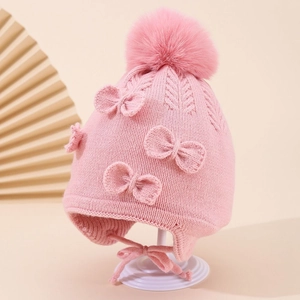 Close-up of pink knit baby hat with three bows and a large fluffy pompom detail