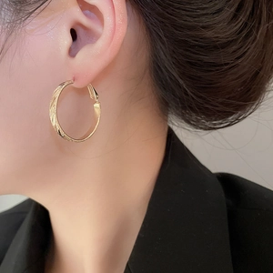 Close-up of textured golden hoop earrings with embossed twill pattern on a female model