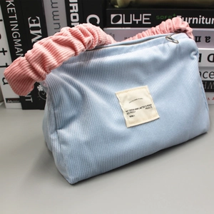 Detail of blue corduroy shoulder bag with pink pleated handle and woven square label