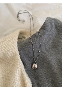 Close-up of a silver teardrop pendant necklace layered on tweed fabric for a chic look