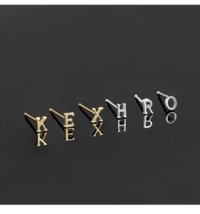 Close-up of gold and silver S925 sterling silver alphabet studs on a black reflective surface