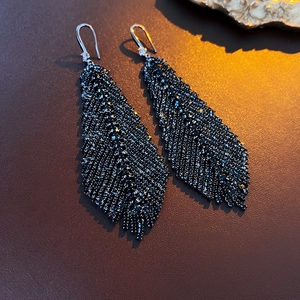 Macro detail of black feather earrings with micro-inlaid crystals and silver ear hooks