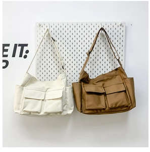 Detail view of large capacity canvas crossbody bags in beige and khaki with dual front pockets
