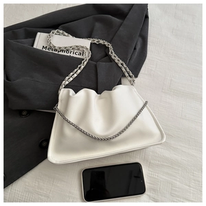 Close-up of white ruched dumpling bag with silver chain straps on black blazer background