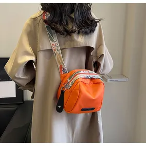 Detail of vibrant orange nylon shell bag with floral wide strap worn over a beige coat