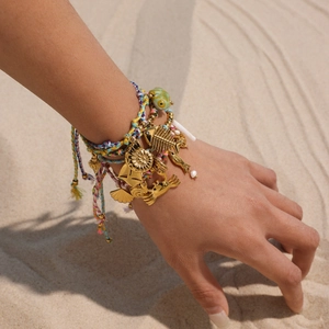 Handmade ocean themed woven bracelet set with golden sea creature charms on sand beach