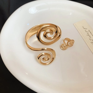 Detail of gold spiral ring and cuff bracelet set on a ceramic tray with sleek finish