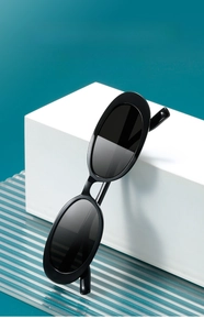 Retro black oval sunglasses on a white geometric stand with a teal background