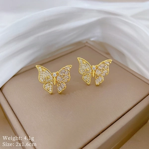 Vue détaillée de boucles d'oreilles papillon dorées avec zircone sur un écrin beige