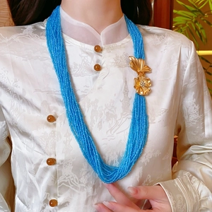 Close-up of multilayered blue beaded necklace featuring golden butterfly and flower charms