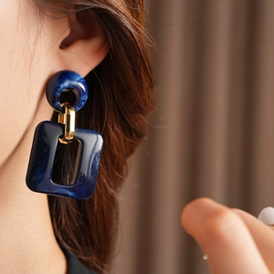 Close-up of geometric navy blue resin earring with gold metal link on female model