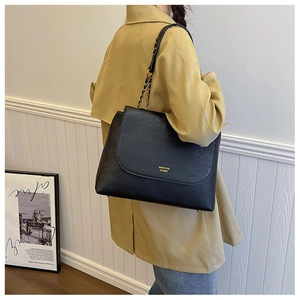 Detail of black leather tote with gold chain strap and logo on a yellow trench coat