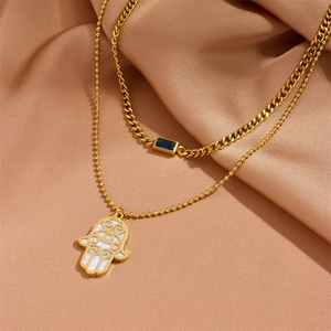 Double-layered gold necklace with Hamsa hand and blue gemstone pendant on champagne silk