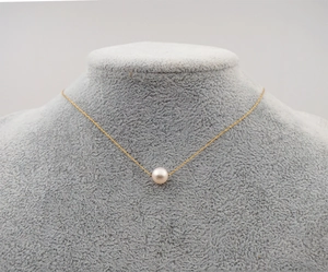 Detailed view of a single pearl pendant on a delicate gold chain shown on a gray stand