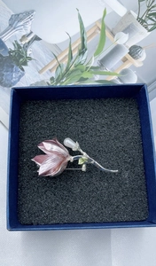 Detail of pink magnolia brooch with silver branches and pearl in a blue jewelry box