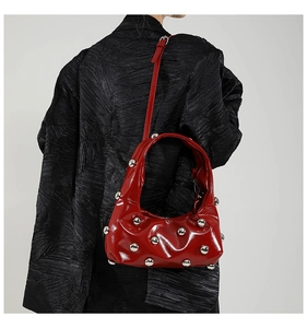 Detail of red patent leather underarm bag with silver rivets worn over a black blazer