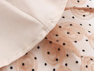 Dettaglio del tessuto a rete beige con eleganti pois neri e motivi a rose 3D