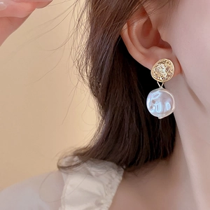 Detailed close-up of a gold textured star earring with an irregular white pearl drop