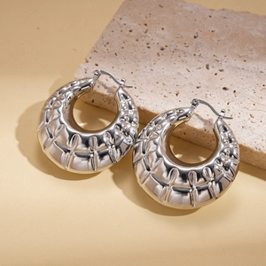 Detail shot of silver metal hoop earring with textured grid pattern on stone background