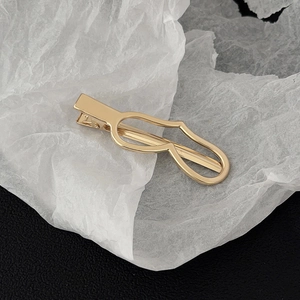 Detail of a curved golden metal duckbill hair clip on a minimalist textured background