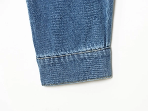 Detailed close-up of blue denim jacket cuff showing twill texture and stitching details