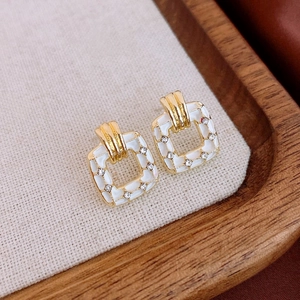 Macro detail of square gold-rimmed earrings with white enamel and sparkling zircon