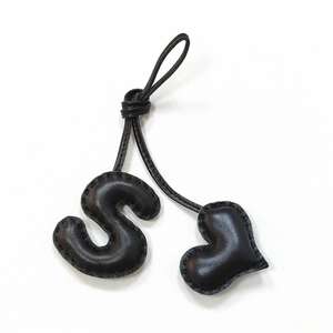 Detailed close-up of handmade black leather bag charm featuring letter S and heart shape