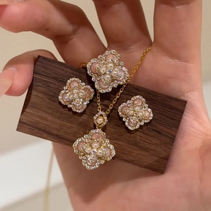 Detailed view of a gold clover jewelry set with pink stones and pearls on dark wood