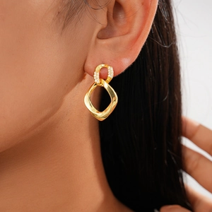 Detail of twisted geometric gold earring with zircon stones worn by a female model