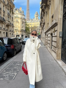 Outdoor street view of a long cream wool coat with high collar and single-breasted detail
