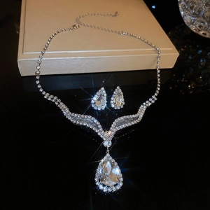 Detailed view of silver necklace and pear-cut crystal earrings on reflective background