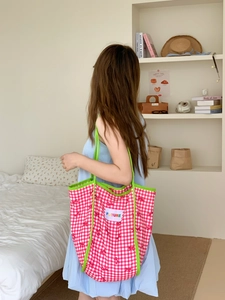 Detail of pink plaid tote bag with green trim and FUTURE patch shown on a shoulder