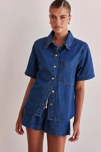 Detail of blue washed denim set showing short sleeve shirt with metal buttons and drawstring shorts