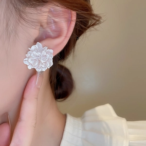 Close-up of elegant white floral stud earrings worn by a model in a minimal setting