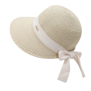 Detail of beige straw sun hat with woven texture, fabric bow and gold logo plaque