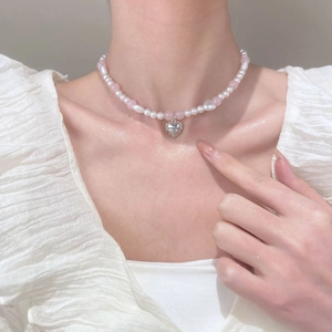 Detail of beaded necklace with white pearls and heart pendant engraved with Sweetie text