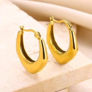 Detailed view of hollow geometric gold stainless steel earrings on beige stone