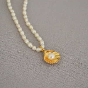 Macro detail of freshwater pearl necklace featuring a golden shell pendant with inset pearl