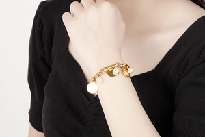Détail d'un bracelet doré avec perles blanches et pendentif disque visage souriant