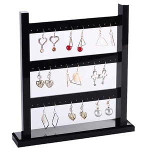 Three-layer black acrylic earring display stand with various stylish earrings on white background