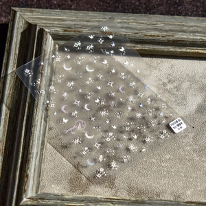 Macro shot of 5D embossed nail stickers featuring white stars, moons and clouds on a board