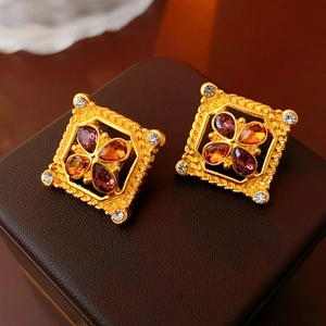 Macro view of vintage gold square earrings with colorful gemstones on leather box