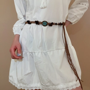 Detail of woven brown waist chain with turquoise metal buckle and wooden beads on white dress