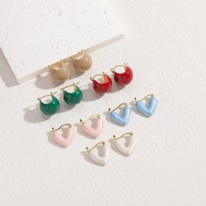 Collection of colorful enamel heart and C-shaped gold hoop earrings on a stone display